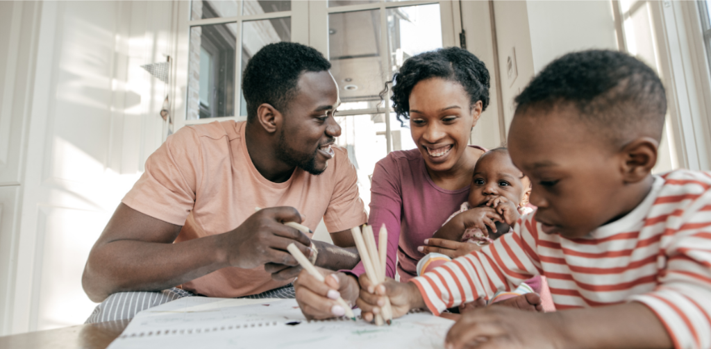 Image depicts a family, including smiling parents holding a baby and a young child coloring.