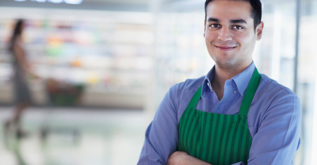Image shows a person who works at  the grocery store giving a subtle smile to the camera with crossed arms.