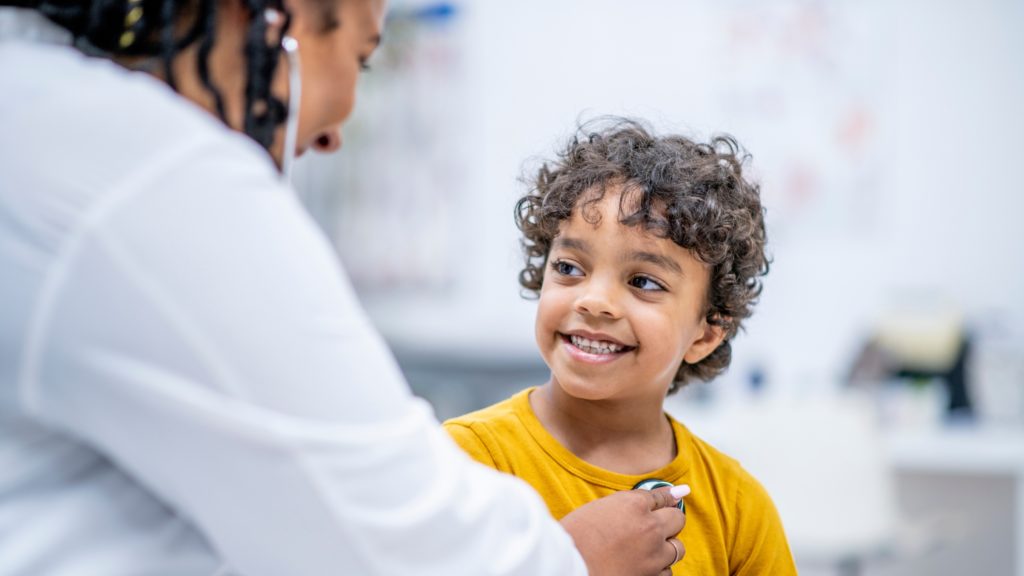 a young child smiles as a doctor places a stethoscope on their chest