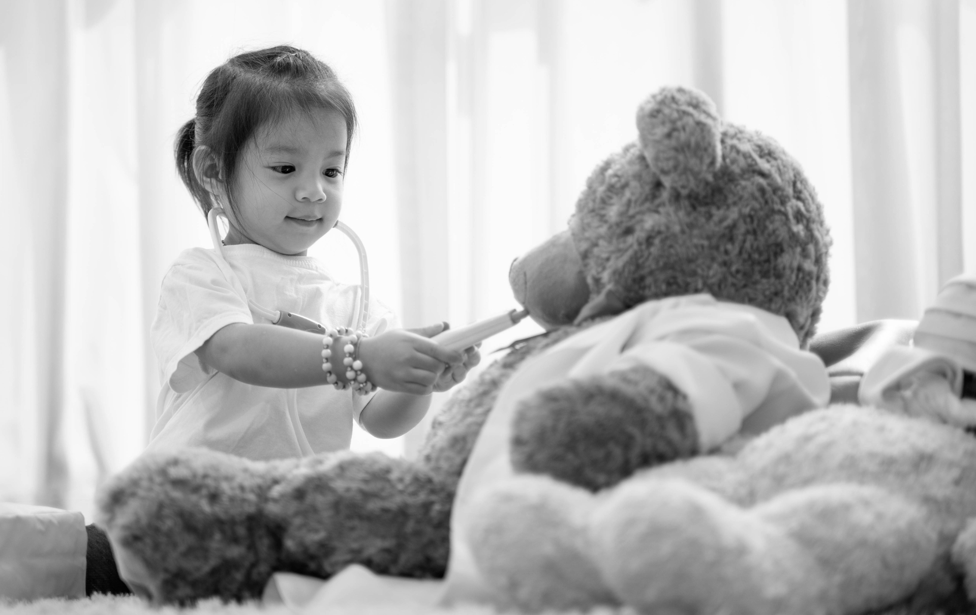 a young child plays doctor with a large teddy bear