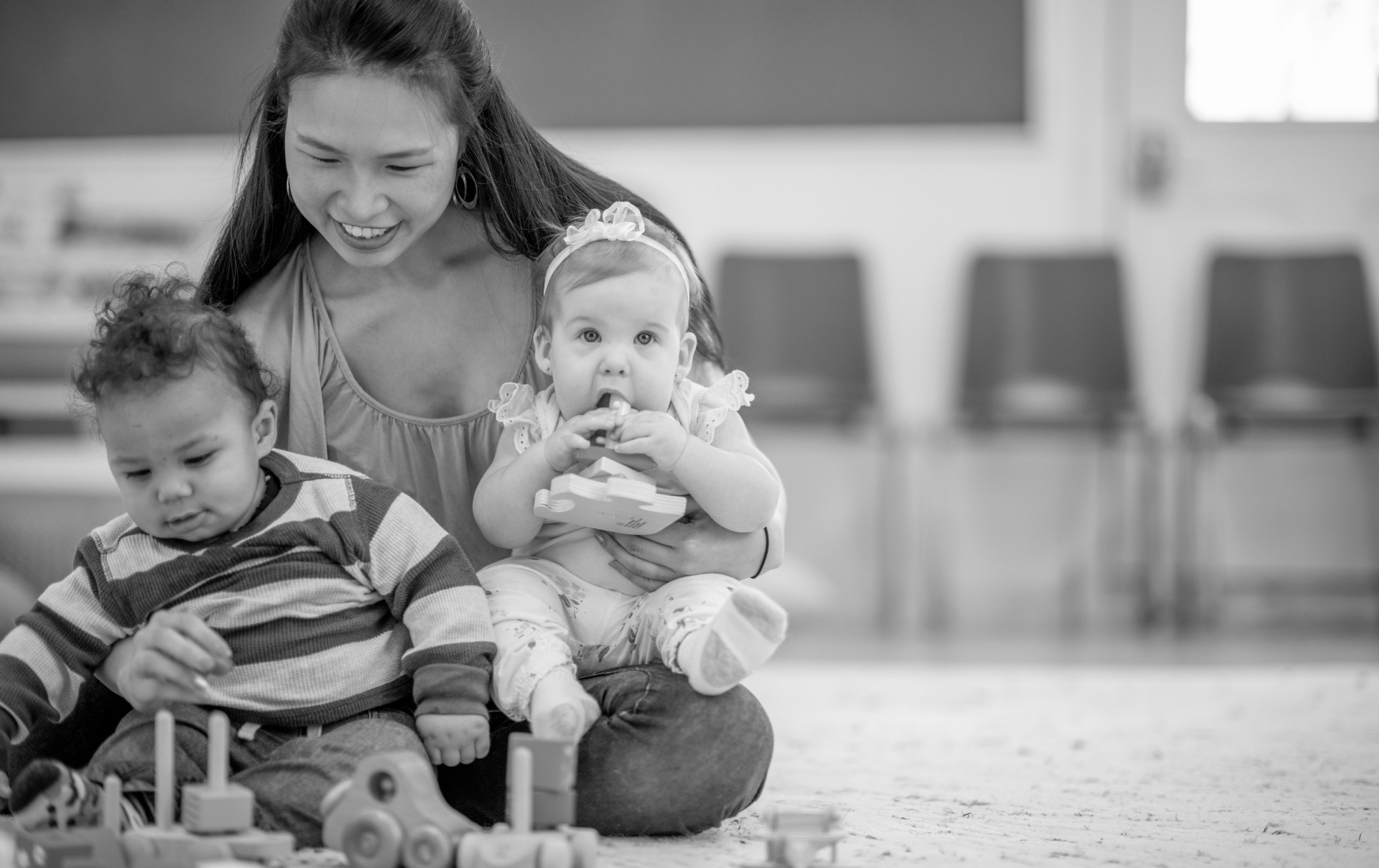 a child care worker sits with 2 babies on their lap while playing with toys