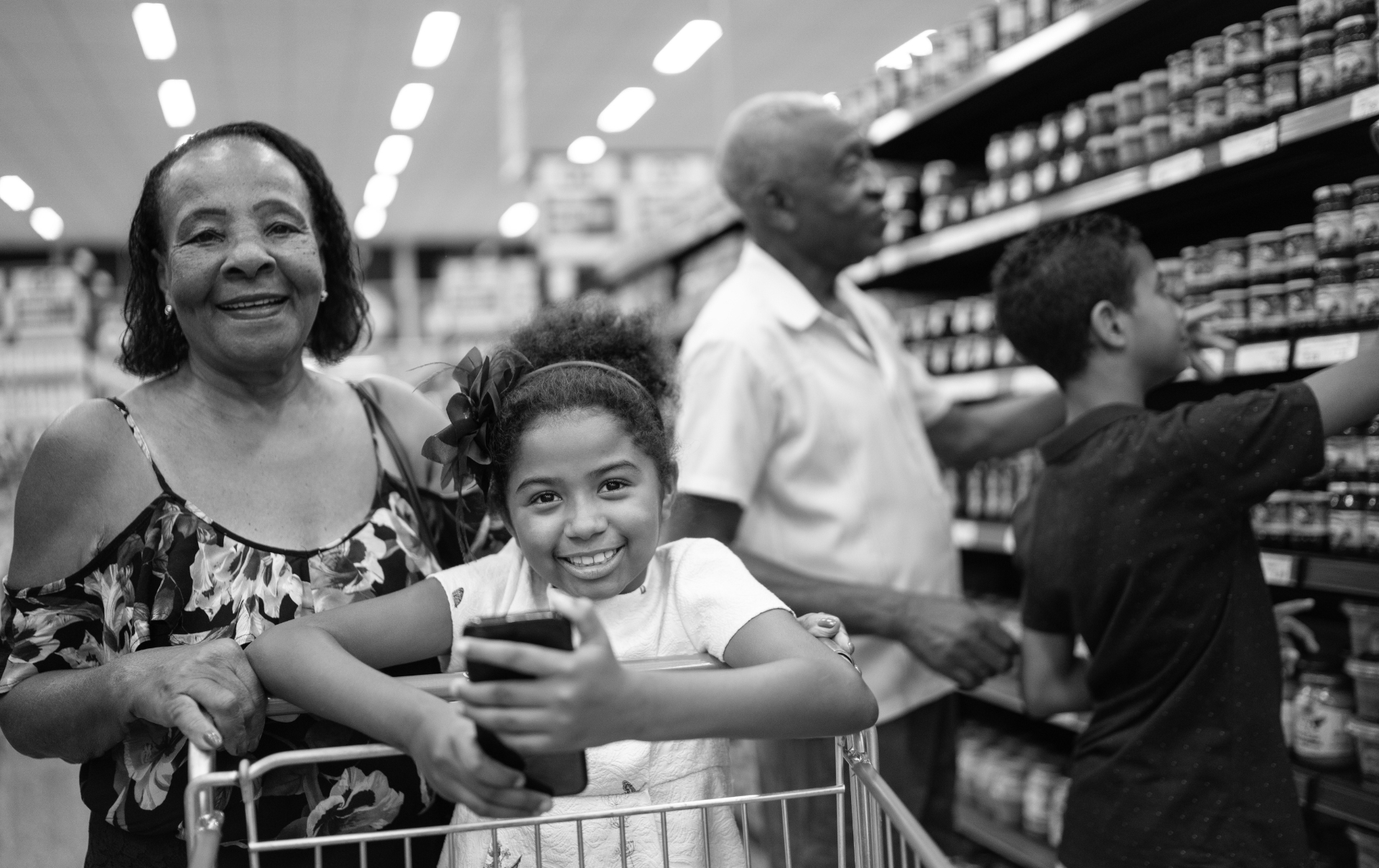 an older women stands behind a little girl who is pushing a grocery cart through the store