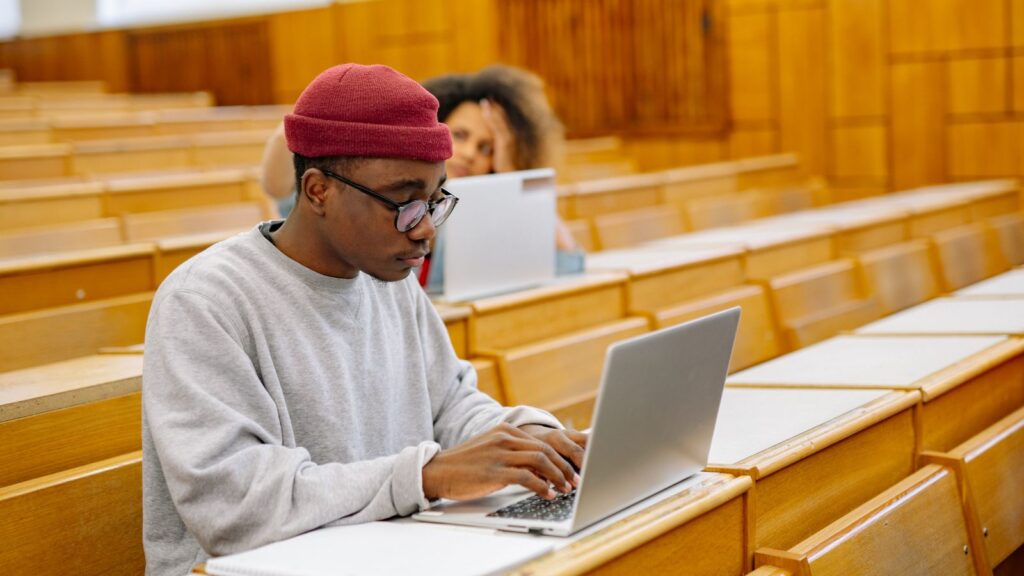A Black college student focuses on his laptop in a university lecture hall, representing the students whose access to higher education is shaped by Virginia's investments in financial aid and HBCU funding